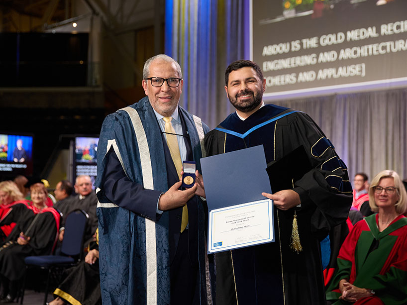 Two people in academic regalia pose for a photo.