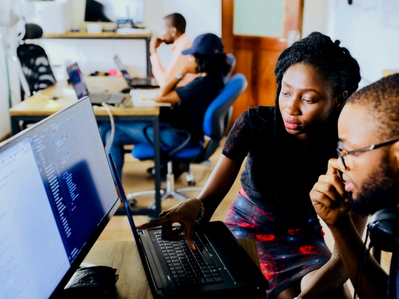 A man and woman look at a computer screen in a computer lab environment.