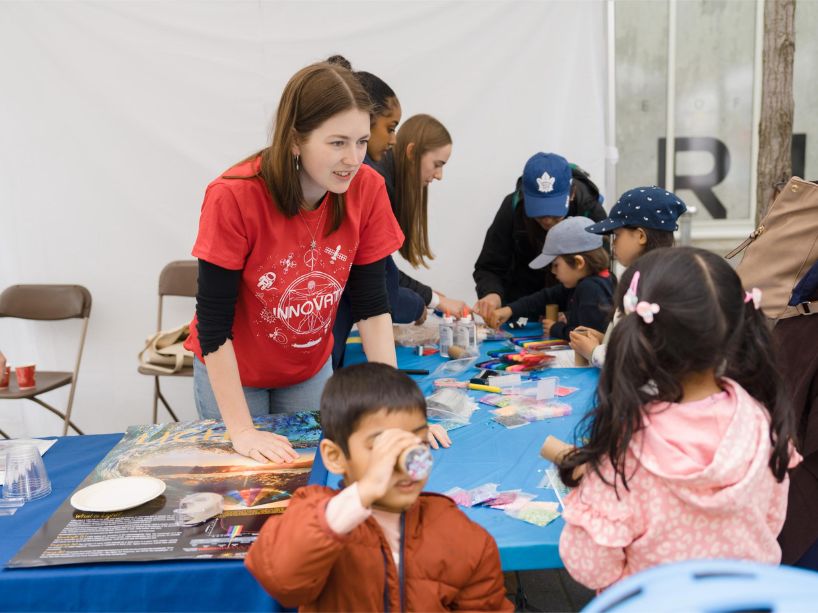 Children around a table creating art projects and learning about STEM-related topics as a volunteer facilitates.