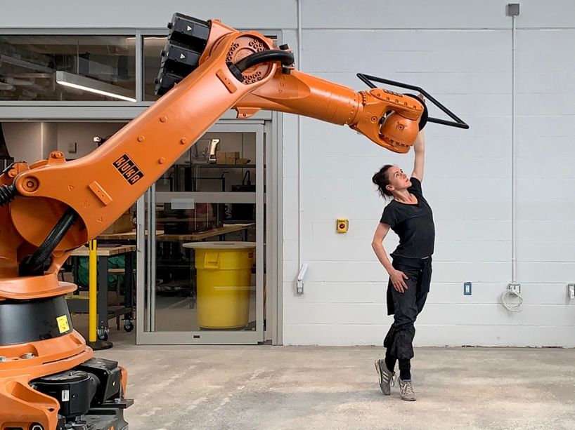 Orange robotic arm with a handle for the dancer to hold in a choreographed and programmed dance together.