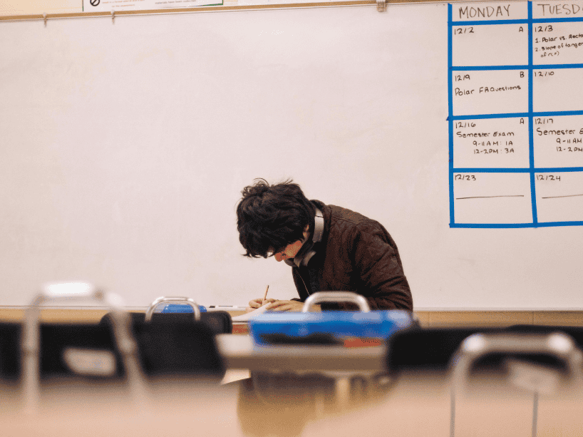 Student writing at a desk with headphones.