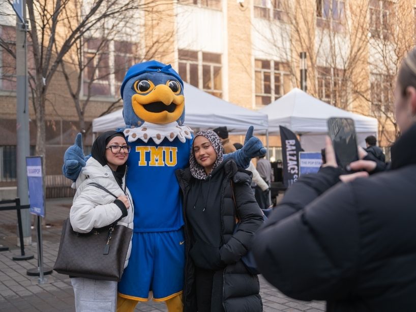 Two people pose for a photo with the TMU mascot.