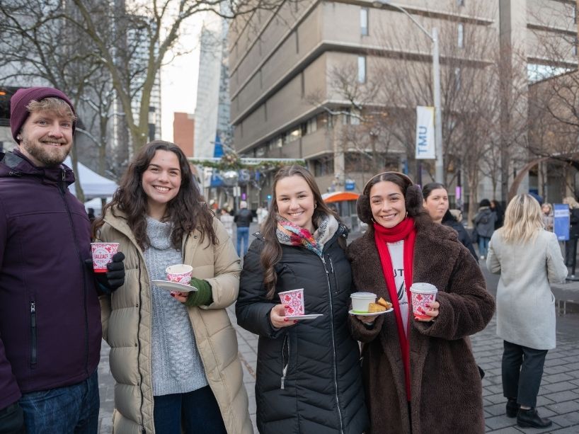  Four people in winter coats pose for a photo while holding warm beverages.