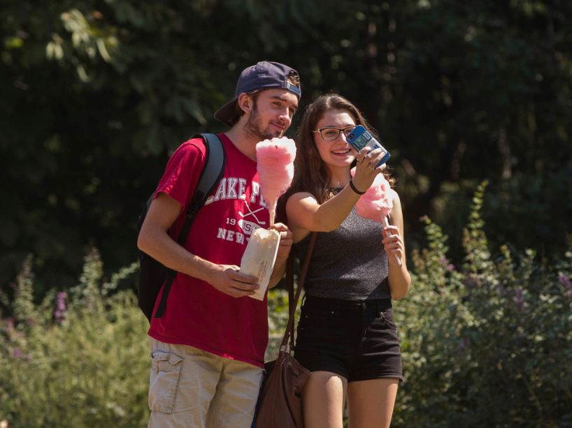 Two students take a selfie while smiling and holding cotton candy in paper cones.
