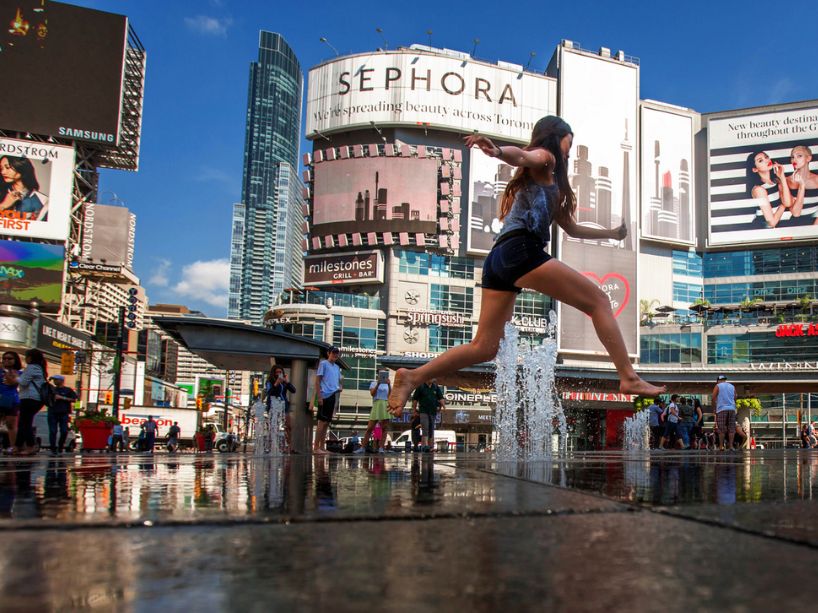 A young woman leaps into the air at the busy downtown Toronto intersection at Yonge and Dundas, surrounded by giant advertisement billboards.