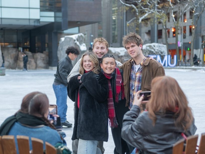 Four students pose for a photo in front of TMU campus’ ice rink.