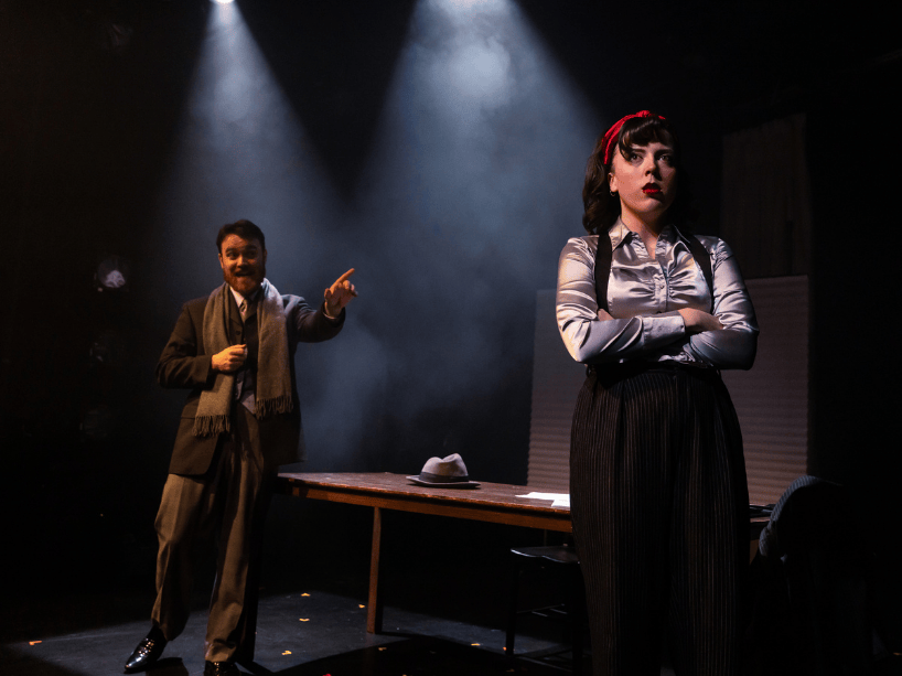 Actor stands with back turned to another performer.