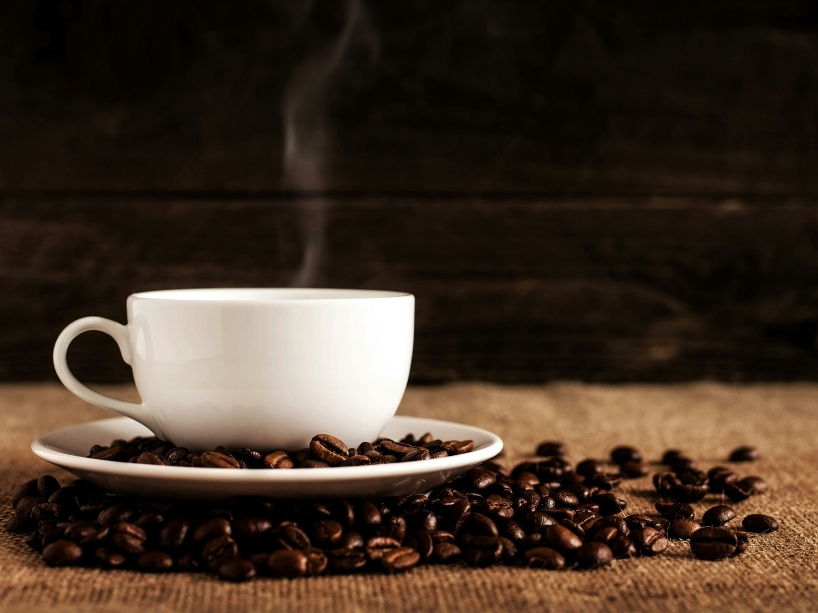 Cup of steaming hot coffee on a saucer filled with coffee beans.
