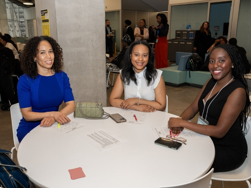 Three people sit at a table with activity materials during a Black History Month event on campus, smiling toward the camera.
