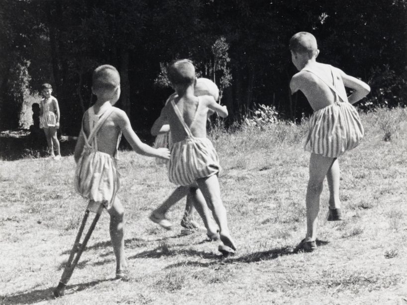 Three children play in a field in a post-World War II black and white photo. 