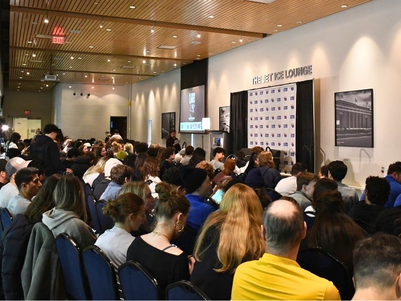 Audience members looking toward a stage and screen.