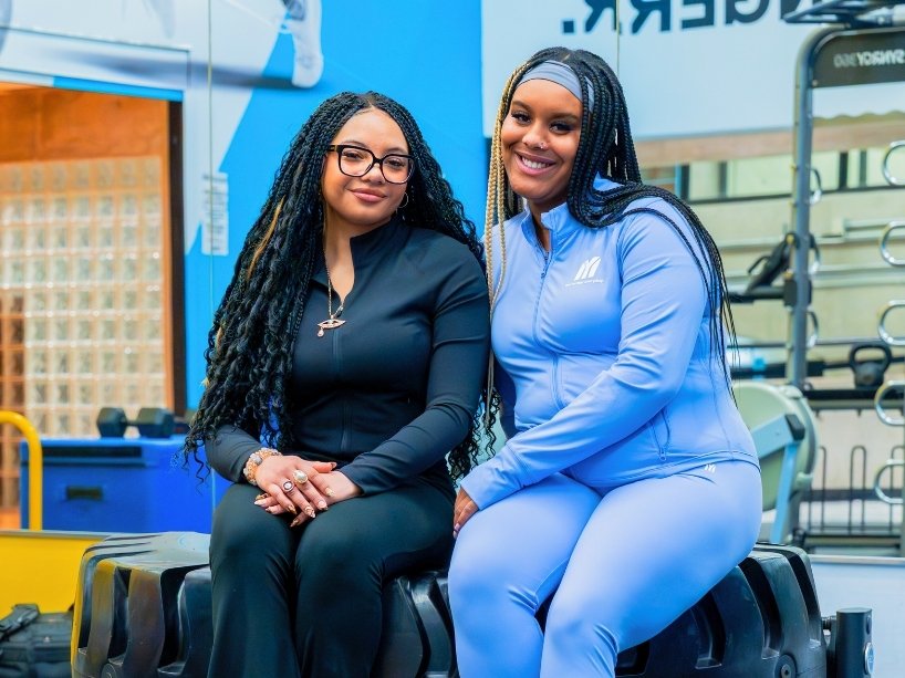 Cami Rabia (left) and Abbygail Baker-Douglas sitting in workout attire in a gym.