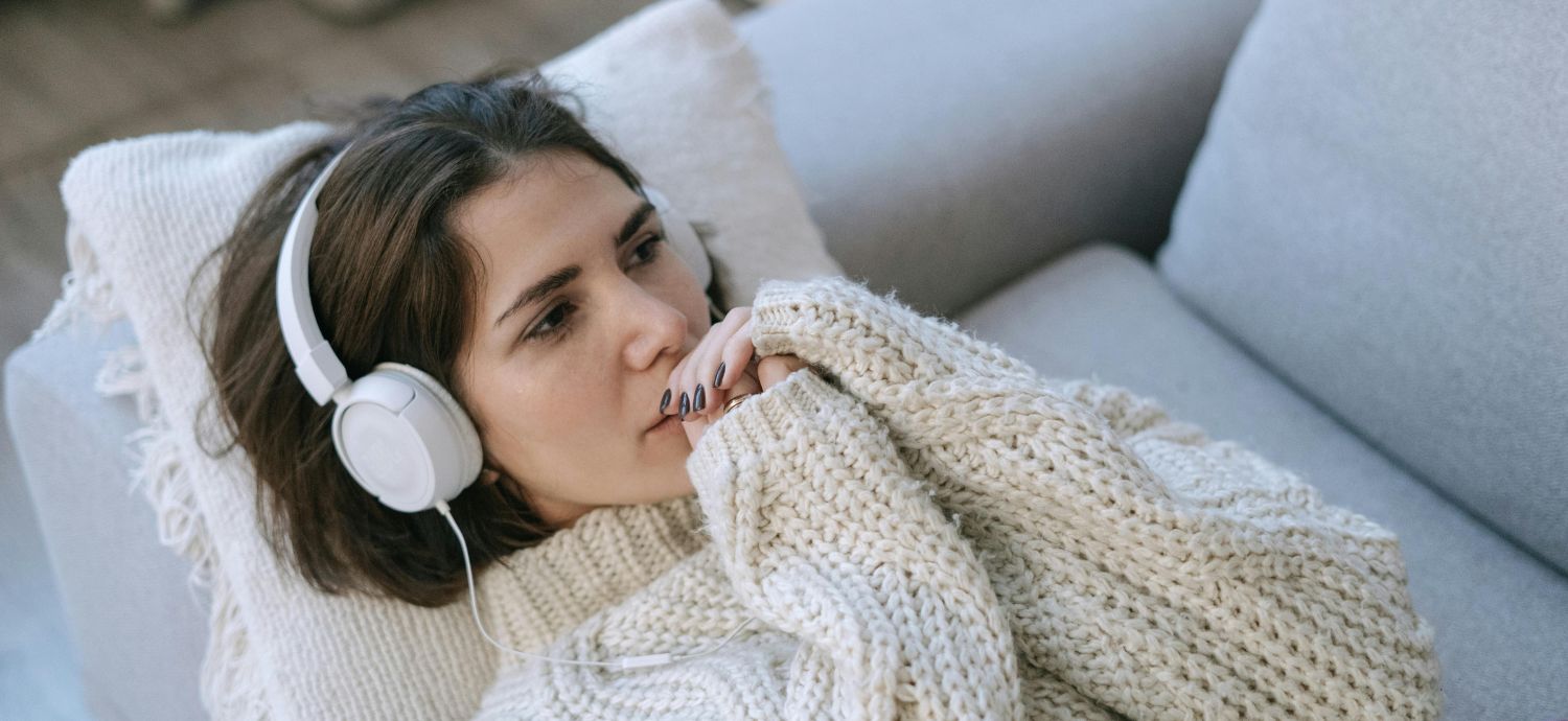A woman lying on a couch and wearing headphones listens to music.