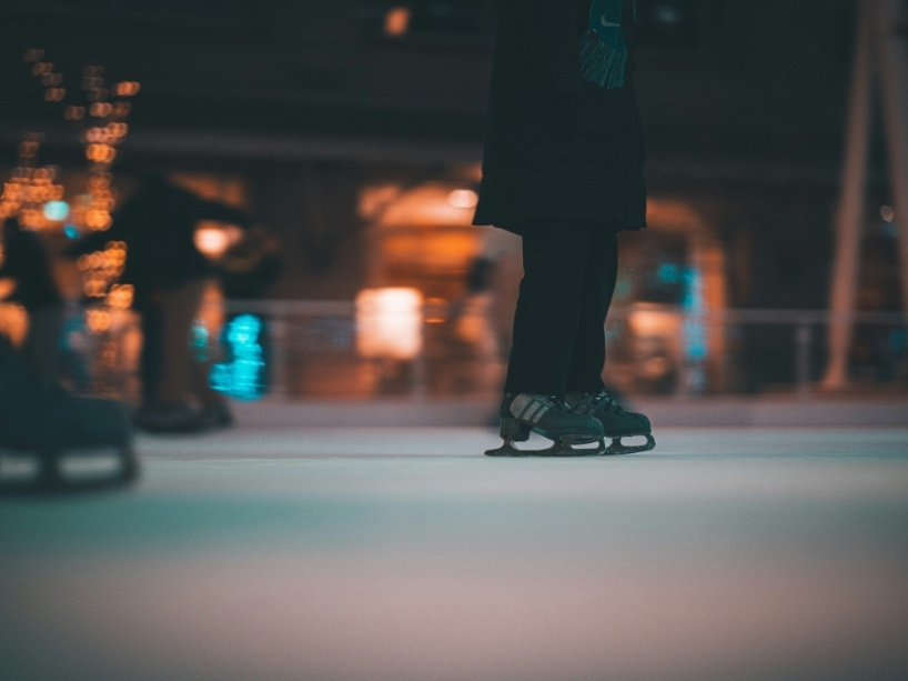 Ice skates are seen on the ice with other skaters in the background.