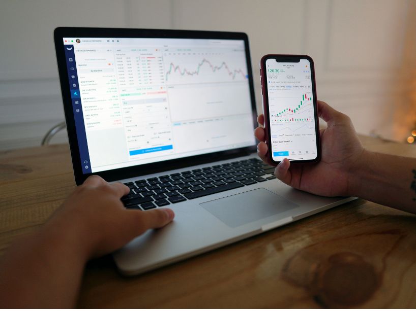 A person is seated in front of a laptop at a desk,  phone in hand, reviewing financial information. 