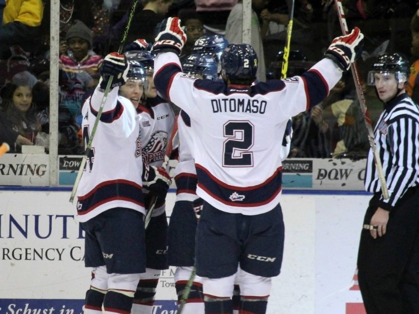 Hockey players come together on the ice with their arms and sticks up in celebration. 