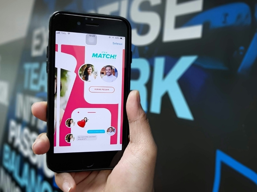 A hand holds up a phone with “It’s a match” seen on the screen along with the image of two profiles connecting.
