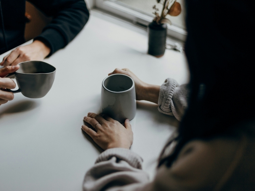 Two cups of coffee held over a table.