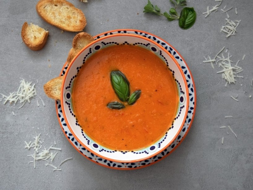 A bowl of soup on a table with bread nearby.