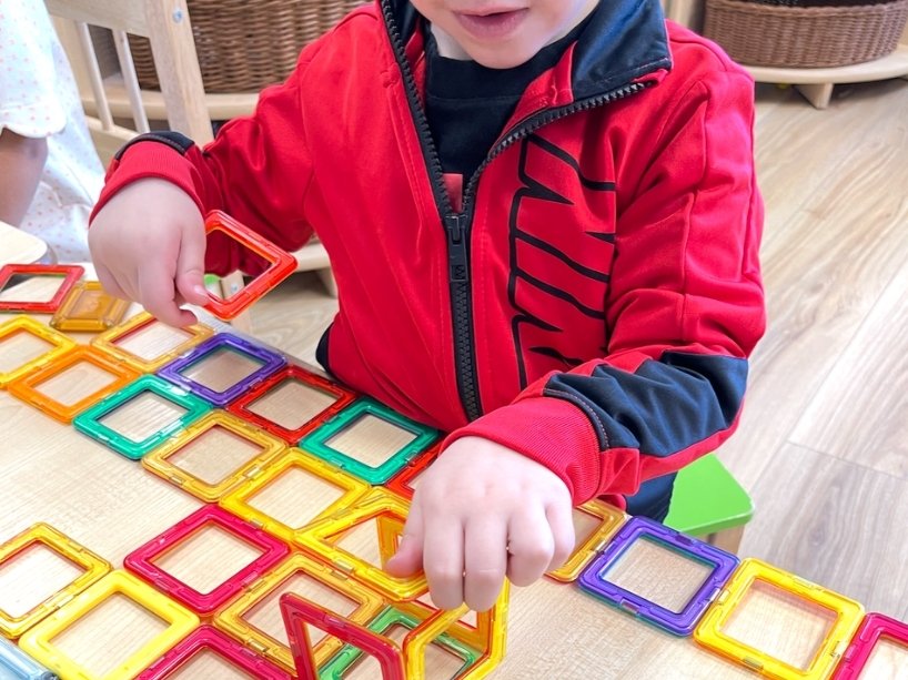 Young child builds structure with magnetic tiles.