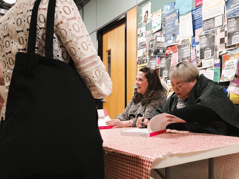 Two women at a table signing books.