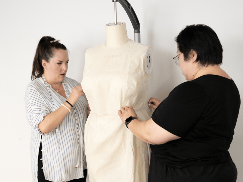 Two women fitting a garment on a mannequin.