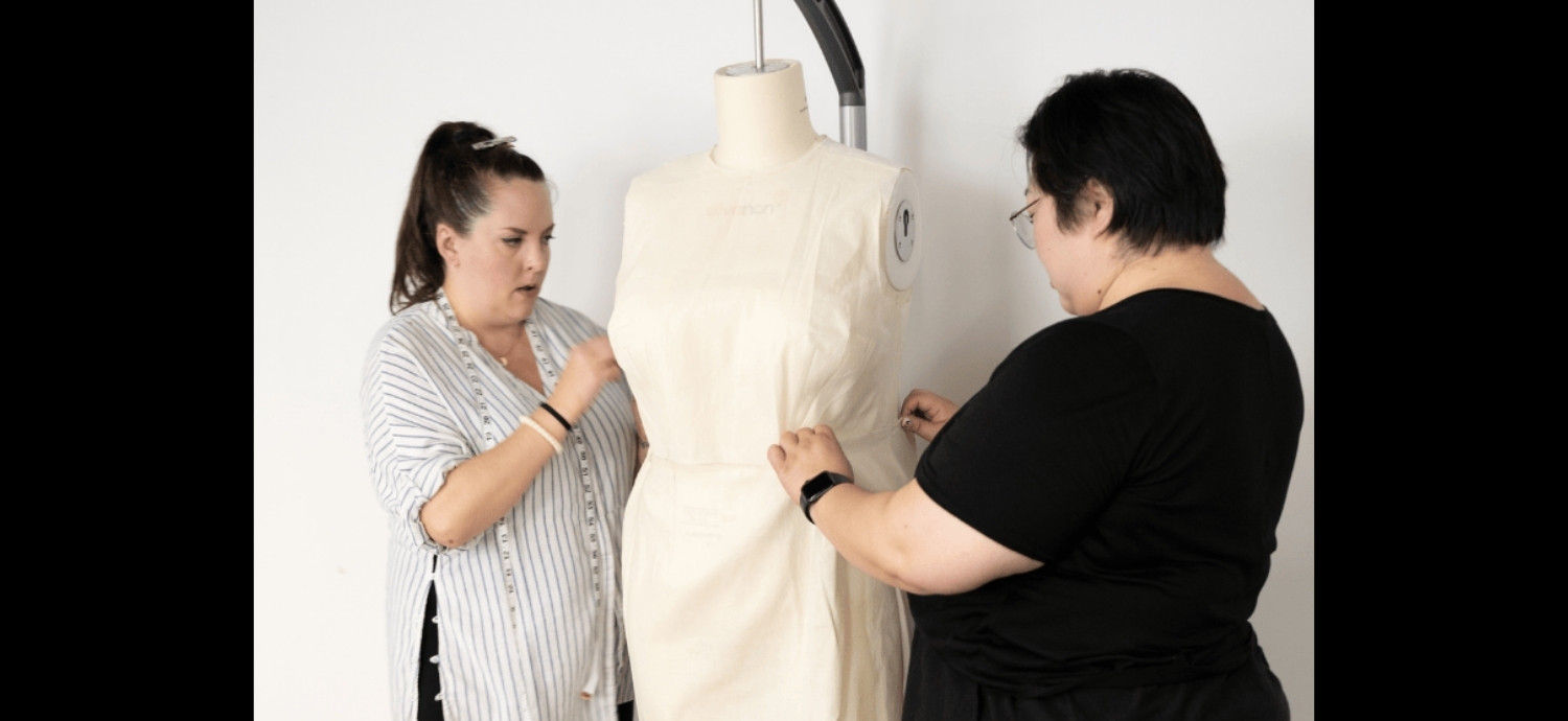 Two women fitting a garment on a mannequin.