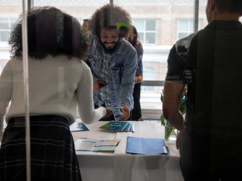People gathered around a table with brochures and pamphlets, with one person handing a brochure to another.