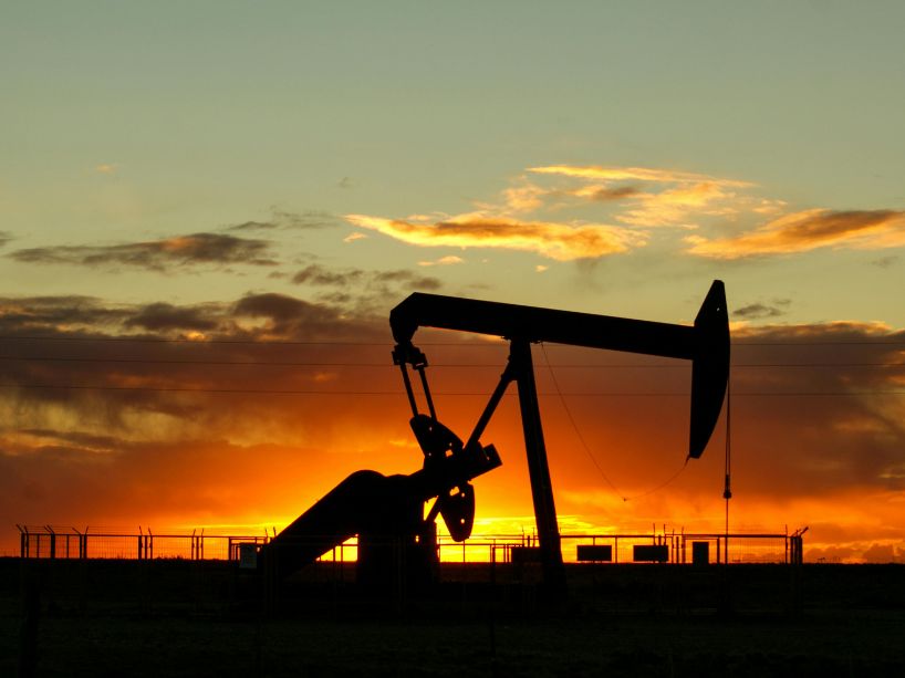 Silhouette of an oil pumpjack against a dramatic sunset sky with orange and yellow clouds.