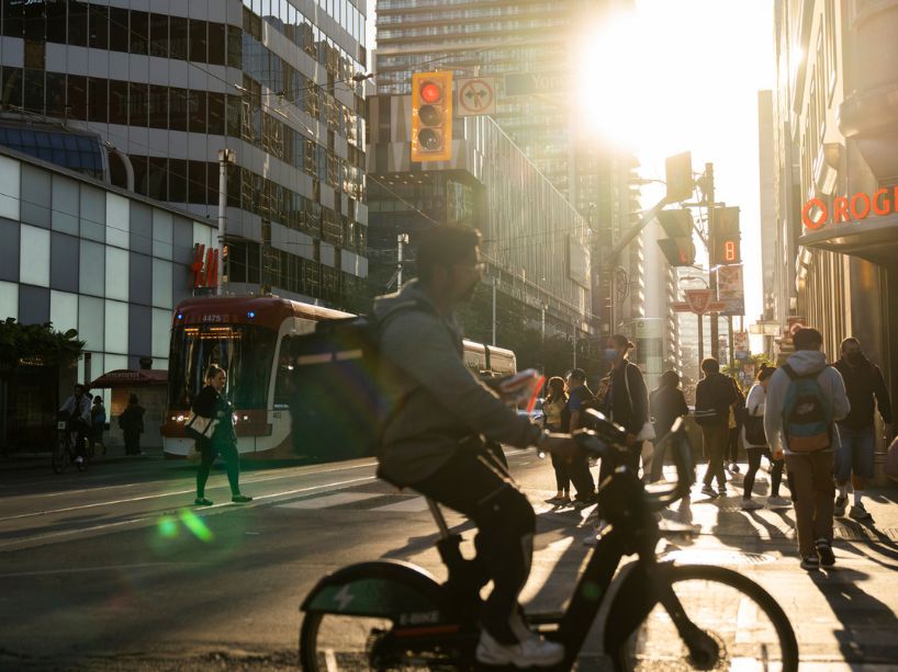Busy Yonge and Dundas intersection showing a streetcar and cyclist on the move, among pedestrians.