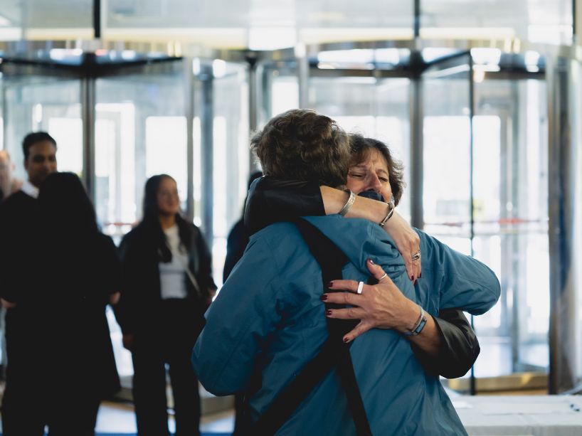 Two women hug; the revolving glass doors of the Student Learning Centre behind them.