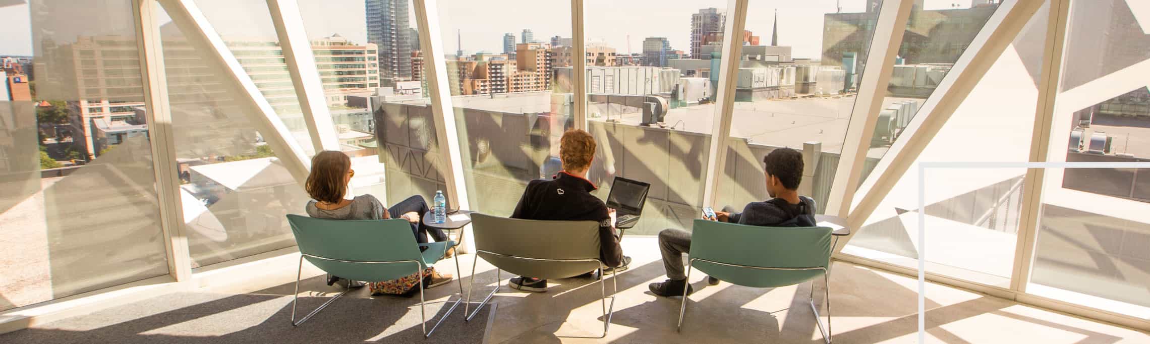 three students sitting inside the Student Learning Centre facing tall windows looking out to the city