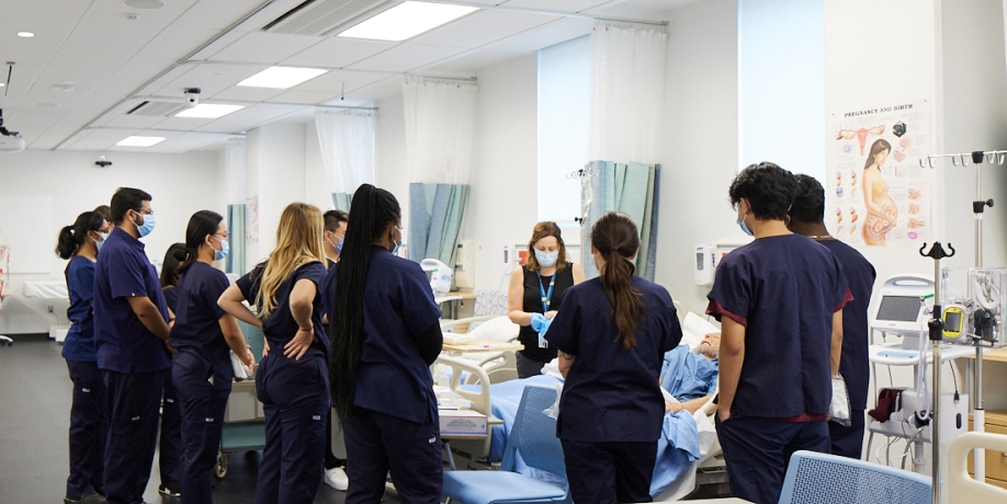 Group of nursing students in the lab gather around a clinical demonstration