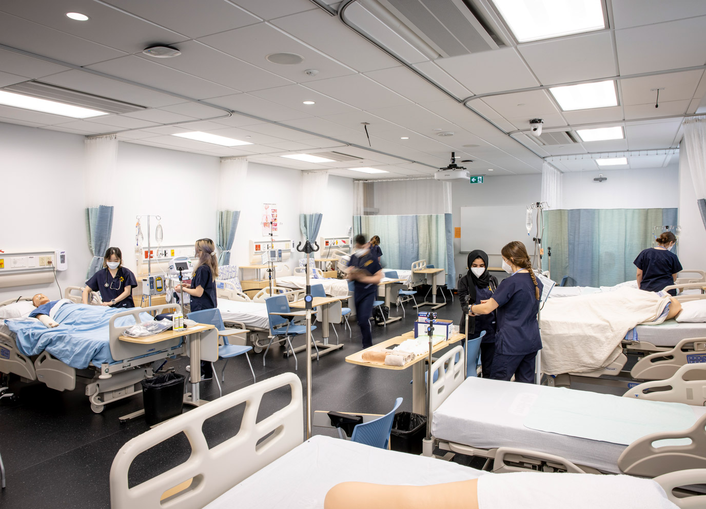 Collaborative Nursing Program students in scrubs work in teams in a medical training room.