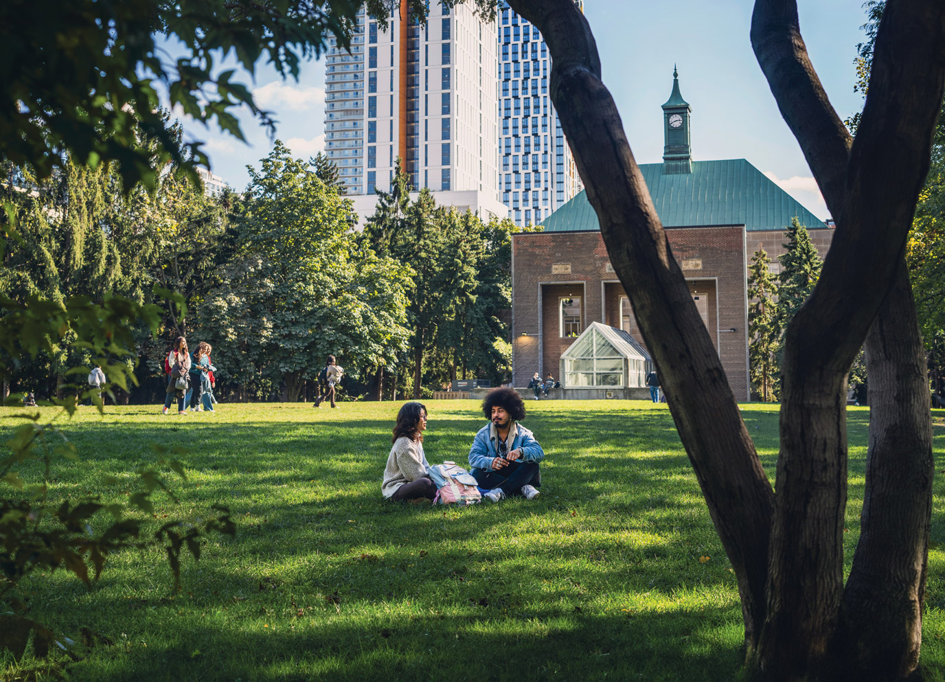 Two students talk while sitting on the green grass of the TMU Quad on a sunny day.