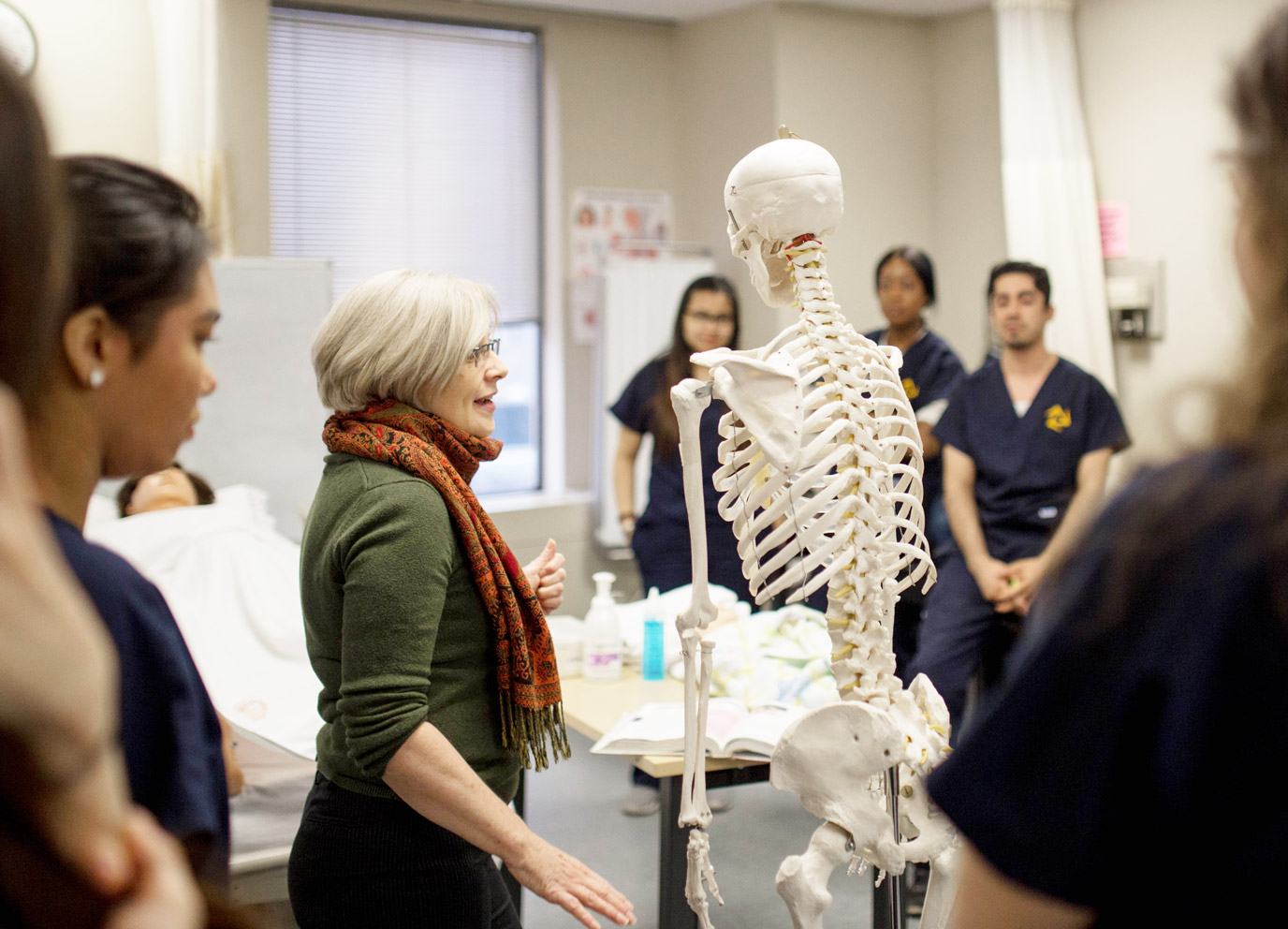 A Collaborative Nursing Program instructor demonstrates a lesson on a skeleton model in a medical training lab.