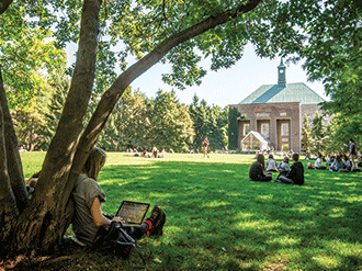 Students working and talking while sitting on the grass in TMU Quad on a sunny day. 