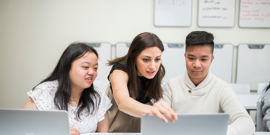 Three students in a classroom looking at a laptop together