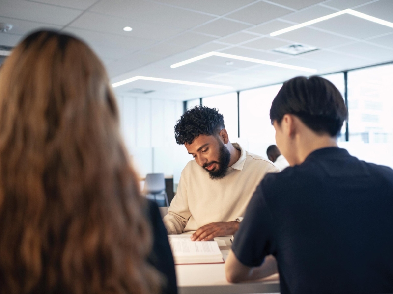 Man with a beard and white-collared shirt studying around a table with two other people
