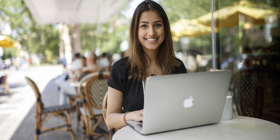 Student smiling while working on laptop sitting in coffeeshop patio