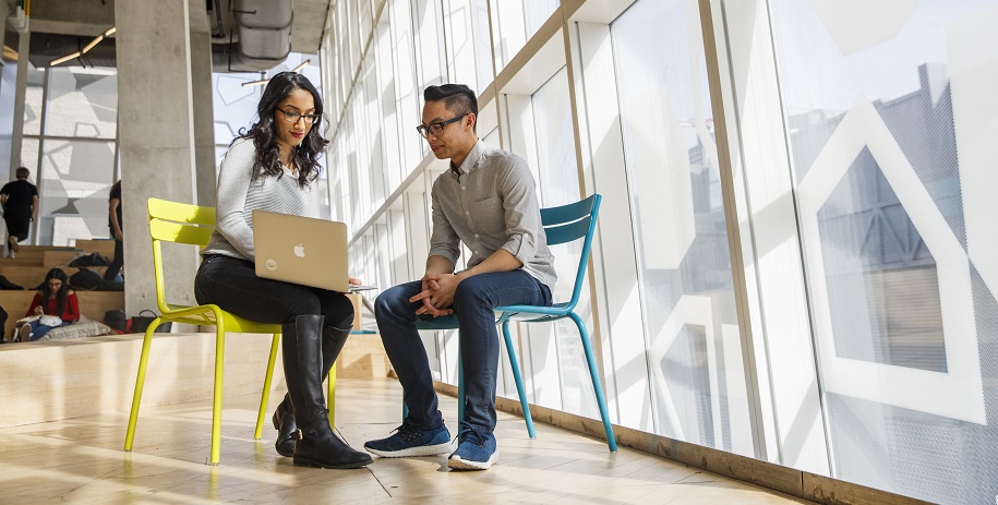 A male and female student sitting together and smiling while looking at laptop