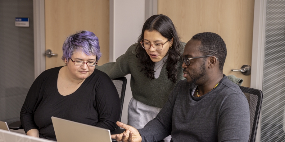 Three master's students gathered around a computer