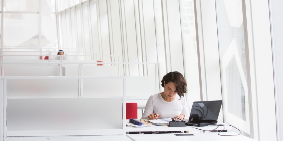 Student working in a white room surrounded by large windows