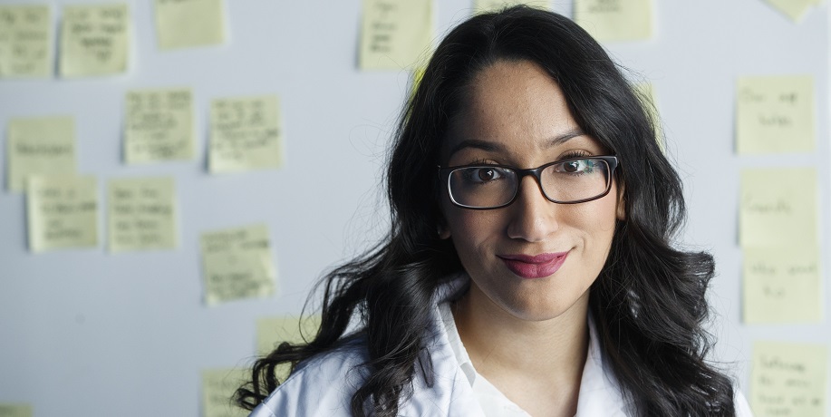 An occupational public health student stands facing the camera, in front of a whiteboard covered in post-it-notes.