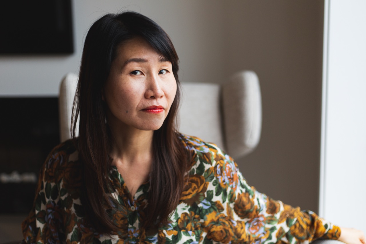 Hanna sits in a floral shirt against a beige background, she is looking at the camera 