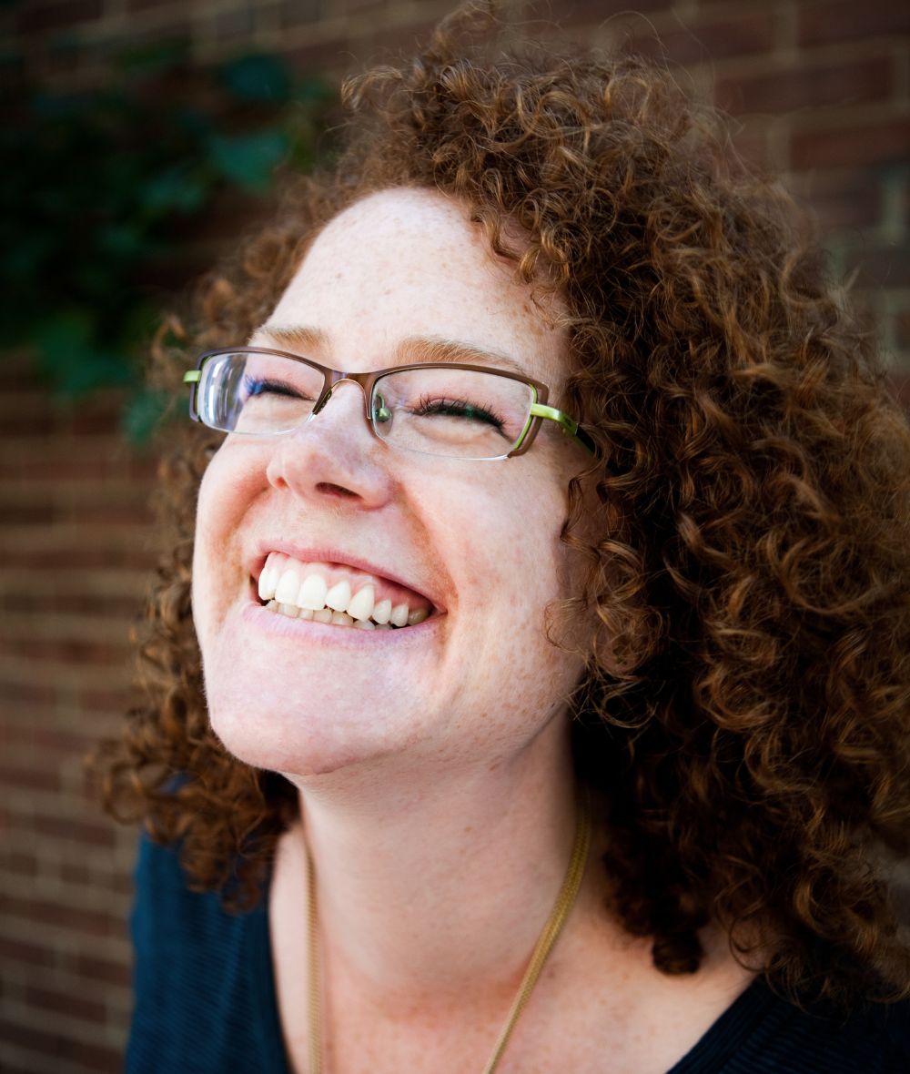 Melanie smiles while looking up towards the sky, her hair is curly and she is wearing glasses