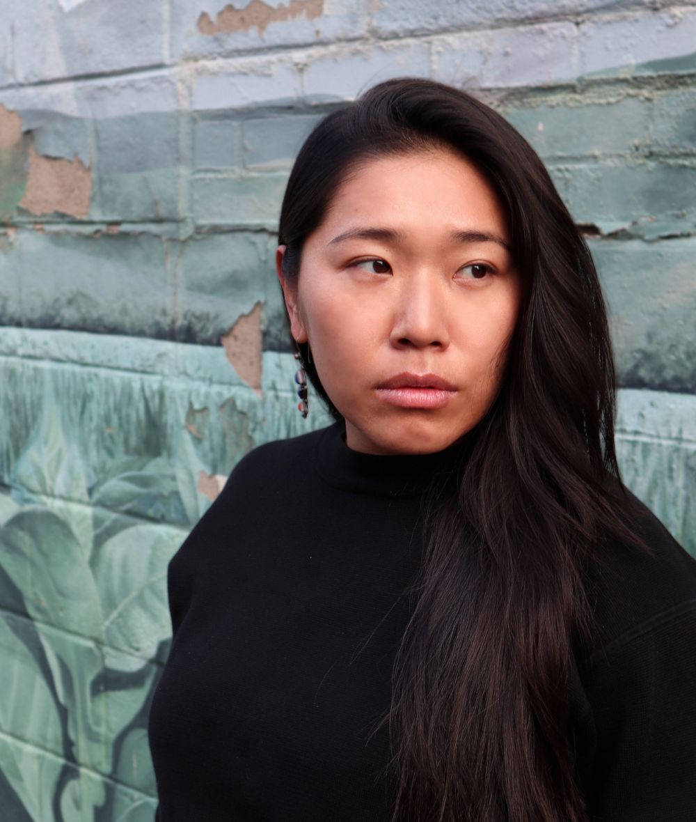 Rinchen looks to her left wearing a black turtleneck sweater against a brick background