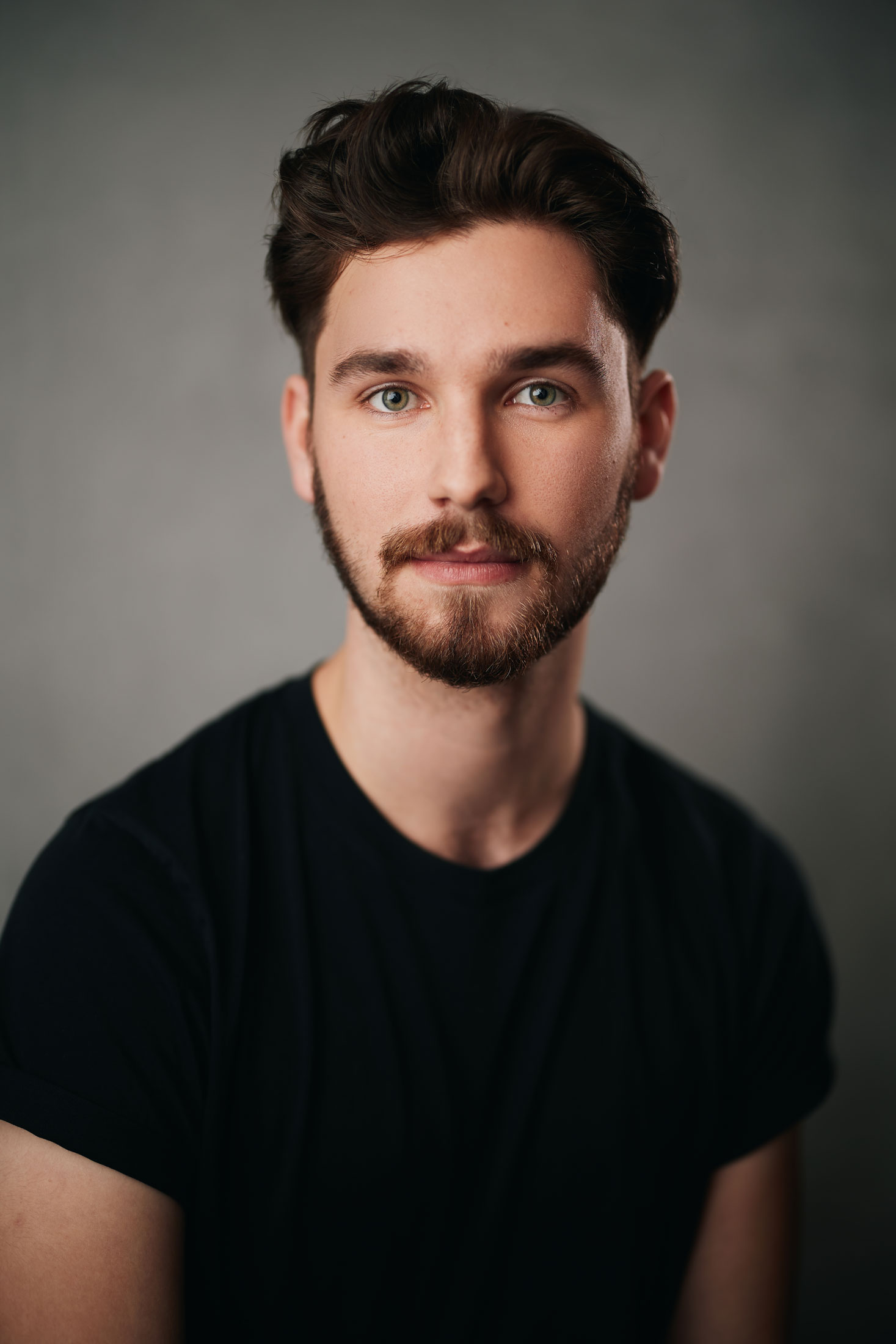 Desmond looks at the camera intently. His thick dark hair stands on his head to an angle. His beard is trimmed close to the face.