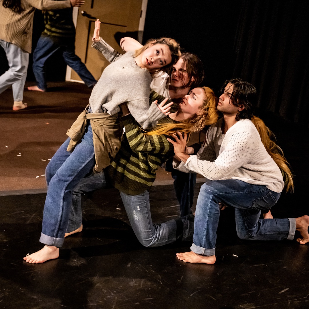 a group of actors on stage, one actress falls dramatically against actors crouched beneath her