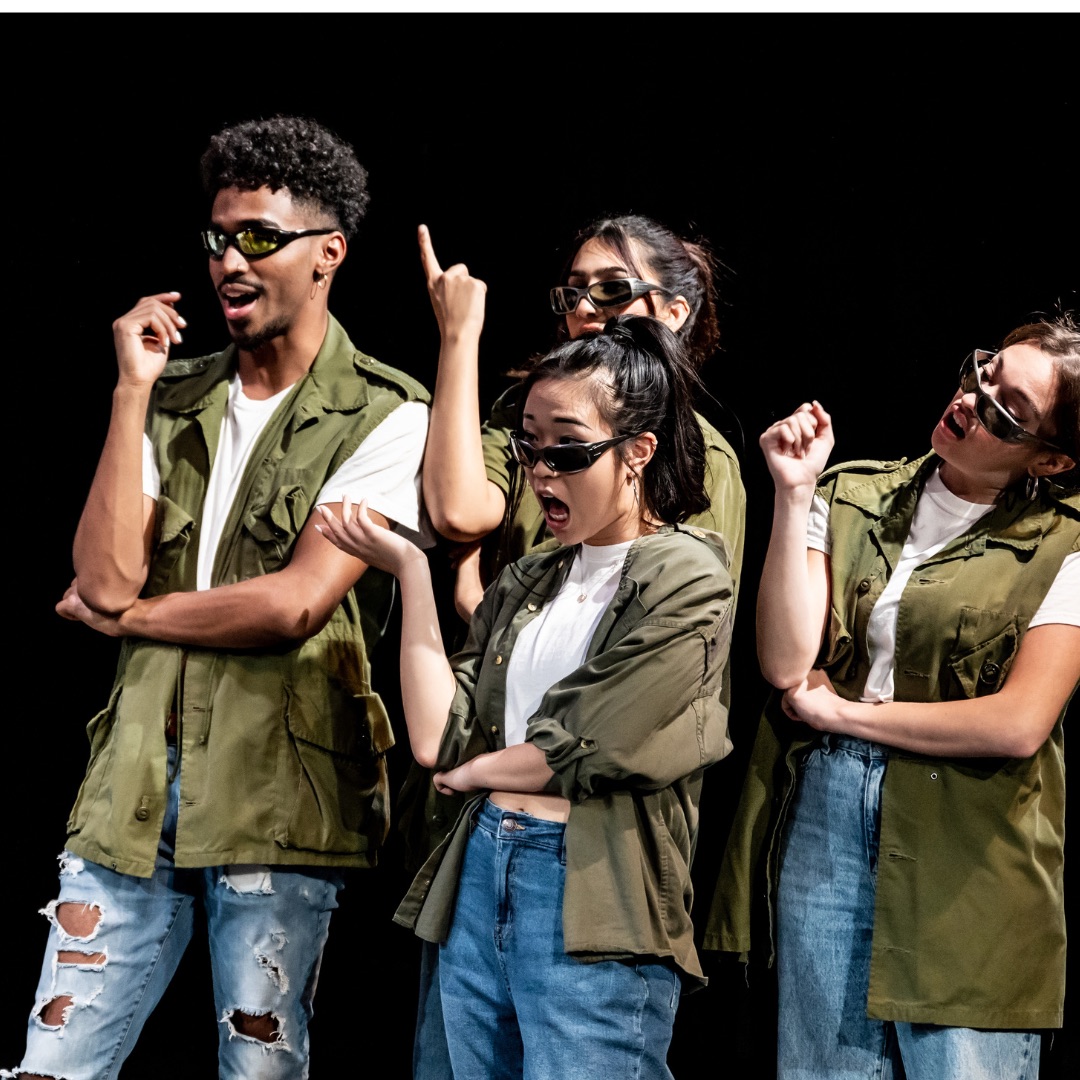 photo of 4 actors all wearing a green vest, jeans, and sunglasses, they look incredulously to the side 